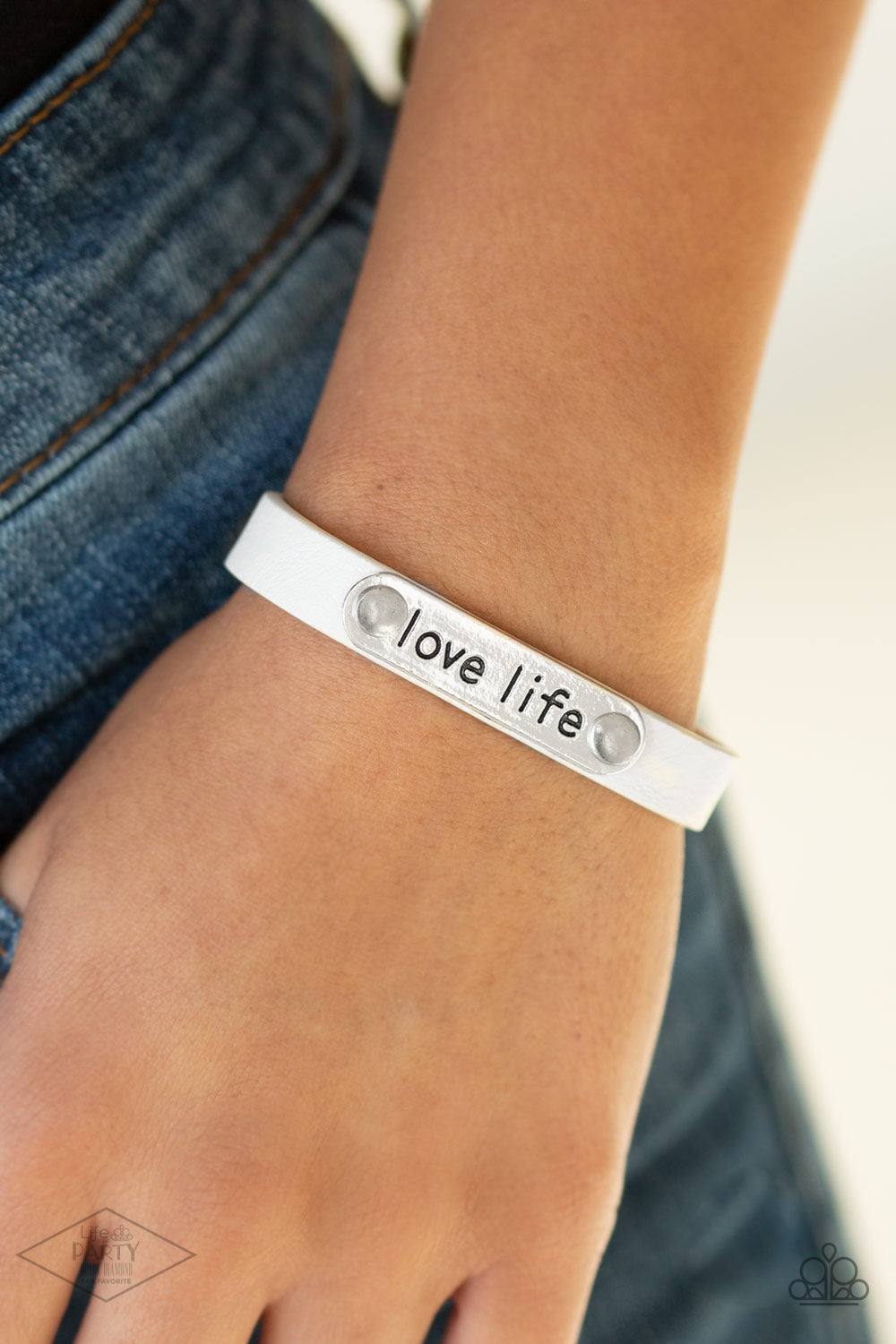 A silver plate engraved with the inspirational phrase “love life” is studded in place along a skinny strip of white leather. Brushed in a shiny finish, the dainty band wraps around the wrist in a simply seasonal style. Features an adjustable snap closure.  Sold as one individual bracelet.  New Kit FANFAVORITE This Fan Favorite is back in the spotlight at the request of our 2020 Life of the Party member with Black Diamond Access, Britney G.