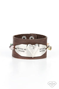 A strand of raw cut multicolored pebbles is threaded through the edges of a curved metal plate, studding the asymmetrical frame in place across the front of a distressed brown leather band. The silver frame is adorned with a hammered silver heart and stamped in the inspiring phrase, "United we stand/Divided we fall." Features an adjustable snap closure