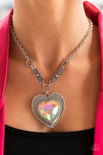 Load image into Gallery viewer, Bordered in spun silver ribbons, an oversized iridescent heart gem is pressed into a silver heart frame below the collar. The flirtatious pendant attaches to silver rings and decorative silver frames dotted in matching iridescent rhinestones, resulting in a dash of vintage inspired romance. Due to its prismatic palette, color may vary. Features an adjustable clasp closure.  Sold as one individual necklace. Includes one pair of matching earrings.
