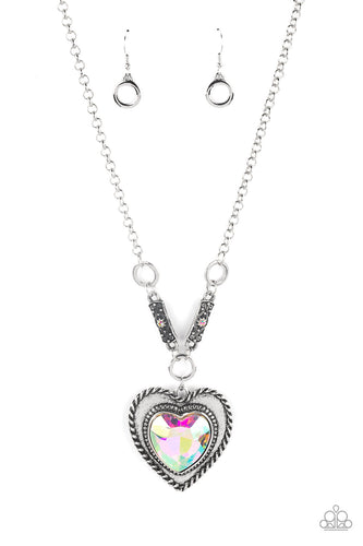 Bordered in spun silver ribbons, an oversized iridescent heart gem is pressed into a silver heart frame below the collar. The flirtatious pendant attaches to silver rings and decorative silver frames dotted in matching iridescent rhinestones, resulting in a dash of vintage inspired romance. Due to its prismatic palette, color may vary. Features an adjustable clasp closure.  Sold as one individual necklace. Includes one pair of matching earrings.